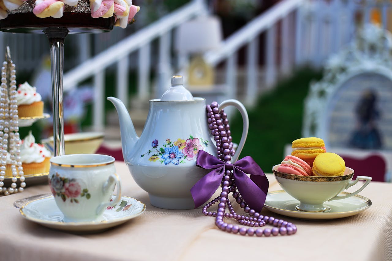 About A beautiful porcelain tea set with cupcakes and macarons, adorned with pearls and lavender ribbon, for an elegant tea time.